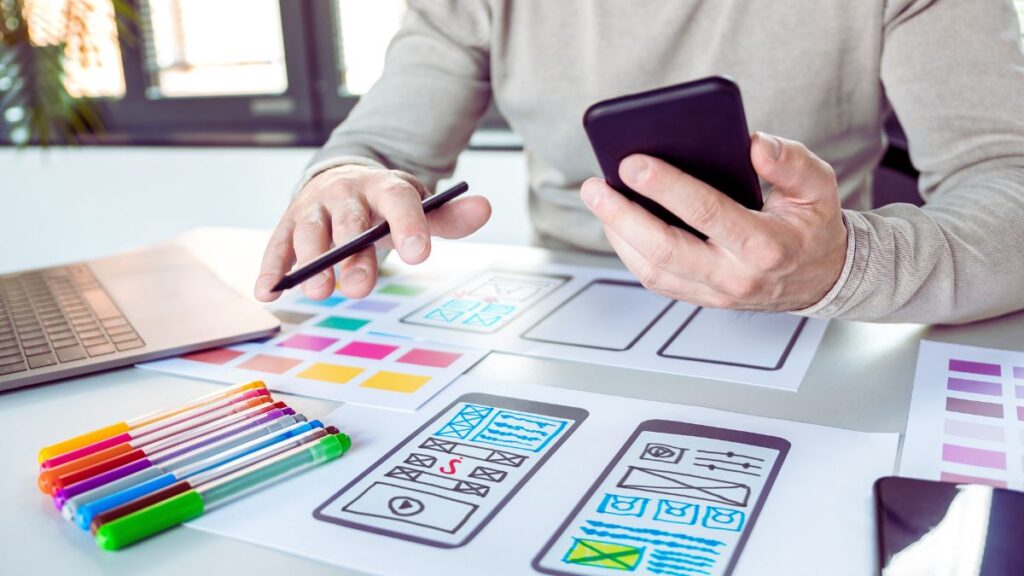 A man designing wireframes of a mobile app on paper sheets.